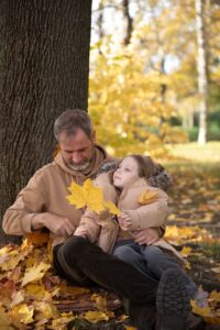 father and daughter enjoying autumn leaves outdoors