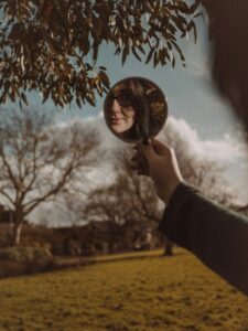 a woman standing in a park with a mirror and looking at her reflection