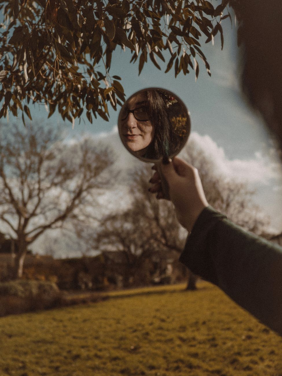 a woman standing in a park with a mirror and looking at her reflection